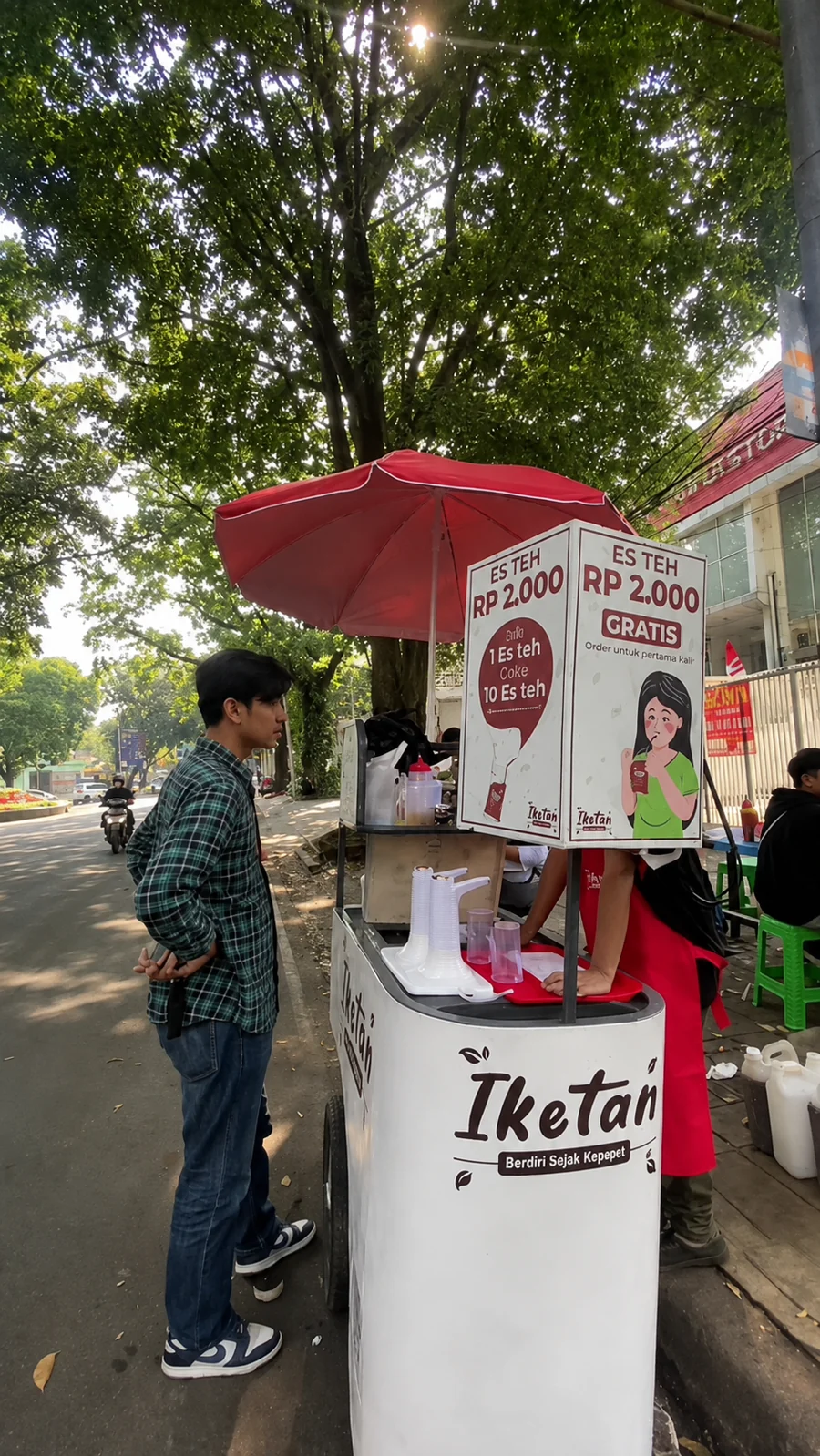 Aktivitas penjualan Iketan di bawah pohon, dengan gerobak dan payung merah